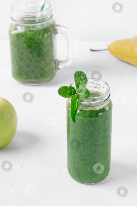 Скачать Зеленый смузи в стеклянных банках на белом столе. Смешайте капусту, яблоко, грушу, апельсиновый сок и воду. фотосток Ozero