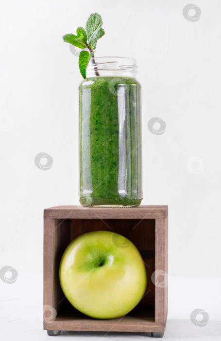 Скачать Зеленый смузи в стеклянной банке поверх деревянной коробки с яблоком внутри на белом фоне. фотосток Ozero