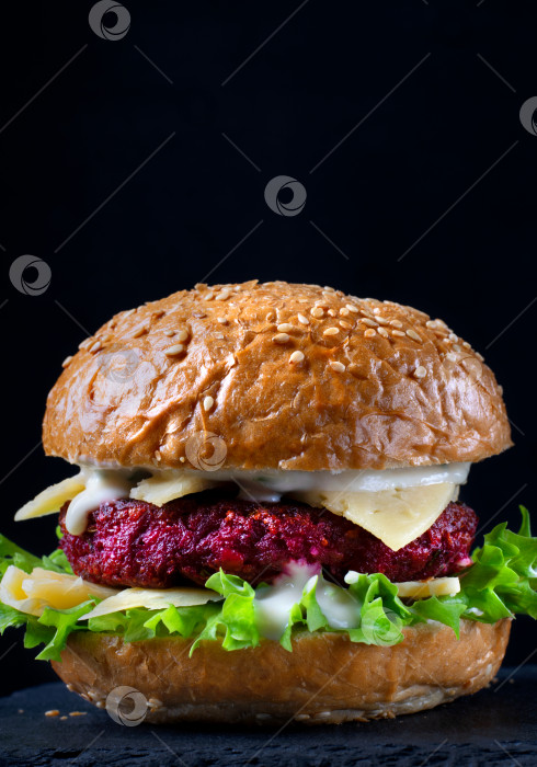 Скачать Бургер из свеклы с листьями салата, сыром и йогуртовым соусом на черном фоне. Здоровая альтернатива без мяса. фотосток Ozero