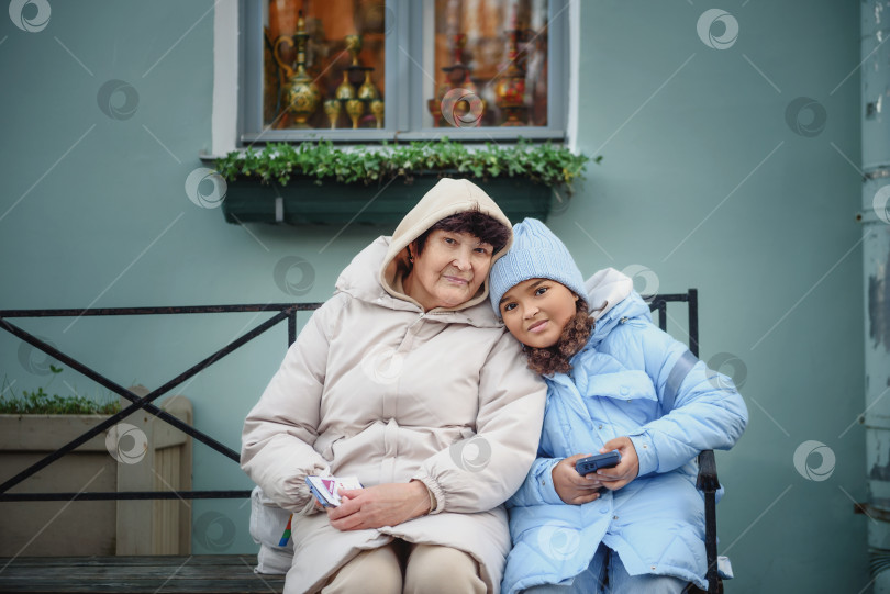 Скачать Внучка и бабушка обнимаются, сидя на скамейке в осеннем лесу фотосток Ozero