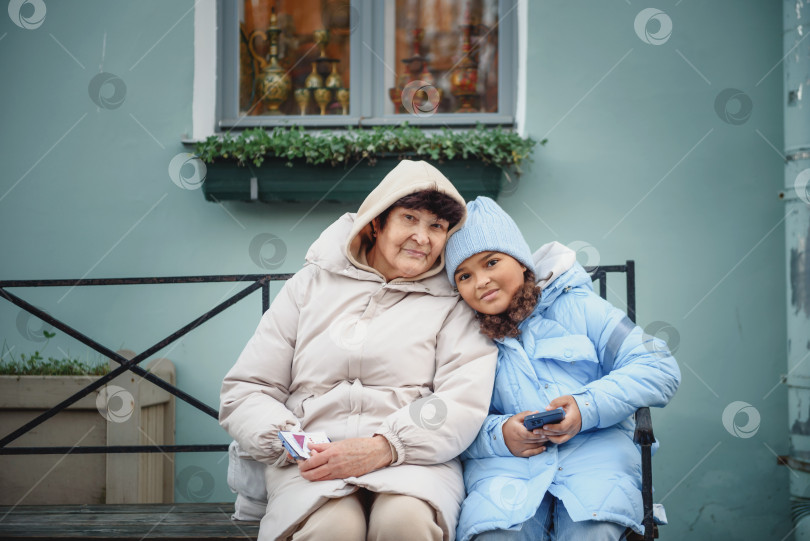 Скачать Внучка и бабушка обнимаются, сидя на скамейке в осеннем лесу фотосток Ozero