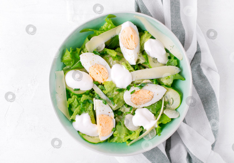 Скачать Салат с яйцами, листьями салата, сыром, огурцом, белой редькой и зеленым луком, политый йогуртом, подается в миске фотосток Ozero