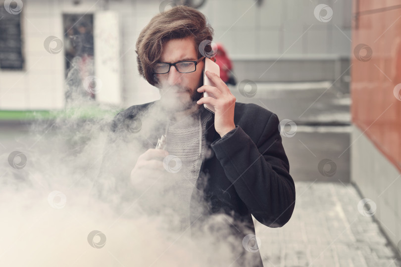 Скачать Мужчина с электронной сигаретой и мобильным телефоном фотосток Ozero
