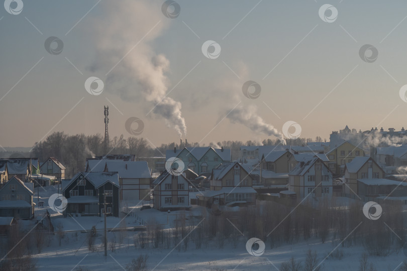 Скачать Дым, поднимающийся из труб домов в зимней деревне под ясным небом фотосток Ozero