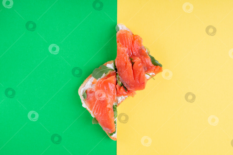 Скачать Тосты с соленой форелью, сливочным сыром и рукколой, разрезанными пополам, на желто-зеленом геометрическом фоне. фотосток Ozero