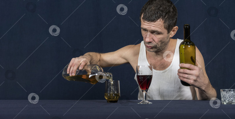 Скачать Пьяный одинокий мужчина в домашней майке сидит за столом. В одной руке он держит бутылку вина, другой наливает алкоголь в бокал. фотосток Ozero