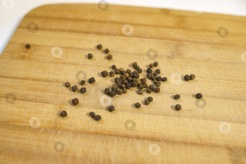 Скачать Горошины черного перца, рассыпанные по деревянной разделочной доске фотосток Ozero