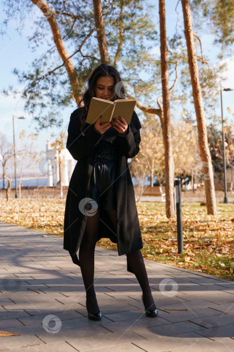 Скачать Девушка в черном пальто прогуливается по парку с книгой в руках фотосток Ozero