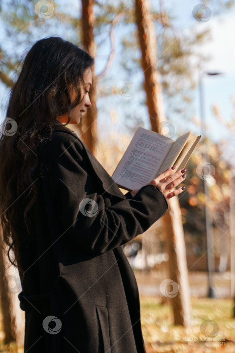 Скачать Девушка в черном пальто прогуливается по парку с книгой в руках фотосток Ozero