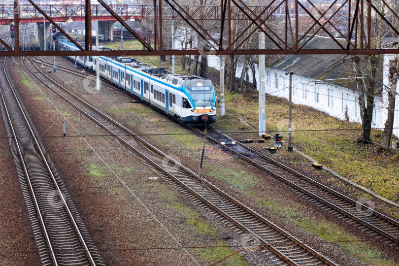 Скачать Беларусь, Минск - 02.01.2025: Бело-голубой поезд движется по рельсам под мостом фотосток Ozero