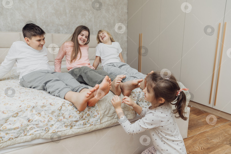 Скачать дети, завернутые в одеяло, щекочут друг другу пятки на кровати. Семья веселится дома. Досуг фотосток Ozero