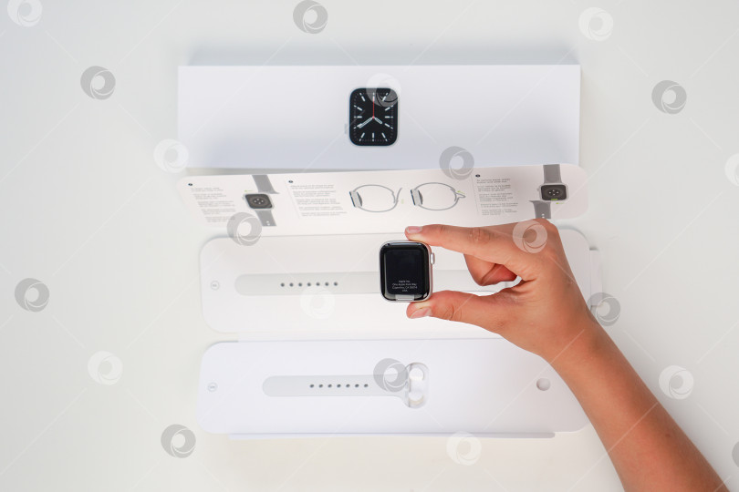 Скачать Распаковка новых Apple Watch Series 6 с серебристым алюминиевым корпусом диаметром 40 мм и белым спортивным ремешком на белом фоне. Шаг пятый. Россия, Татарстан, 10 июня 2021 года фотосток Ozero