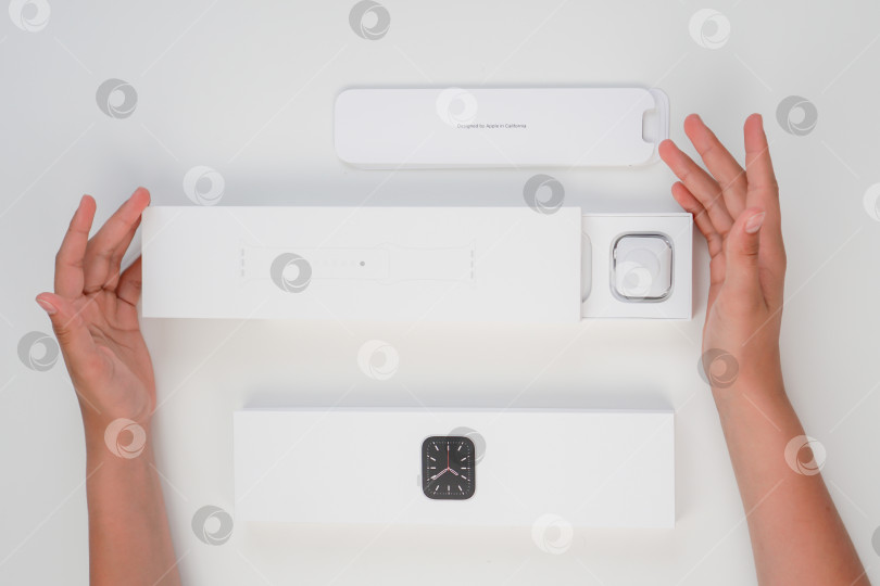 Скачать Распаковка новых Apple Watch Series 6 с корпусом из серебристого алюминия диаметром 40 мм и белым спортивным ремешком на белом фоне. Шаг второй. Россия, Татарстан, 10 июня 2021 года фотосток Ozero