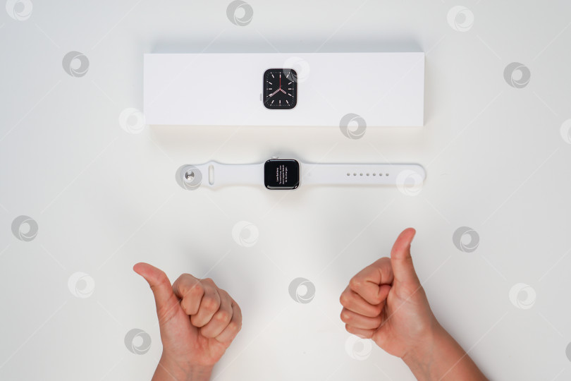 Скачать Распаковка новых Apple Watch Series 6 с серебристым алюминиевым корпусом диаметром 40 мм и белым спортивным ремешком на белом фоне. Шаг седьмой. Россия, Татарстан, 10 июня 2021 года фотосток Ozero