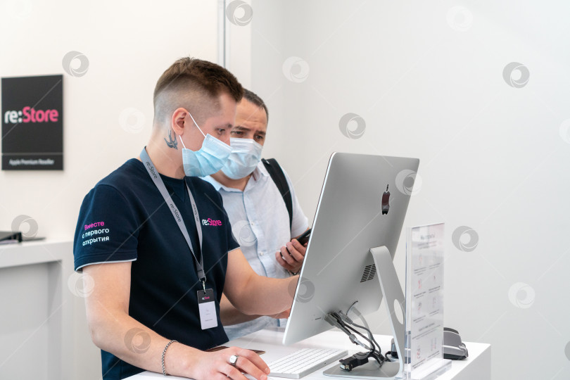 Скачать сотрудник re:store genius помогает покупателю с покупкой во время запуска продаж iPhone в магазине компании в России. Россия, Татарстан, 10 июня 2021 г. фотосток Ozero