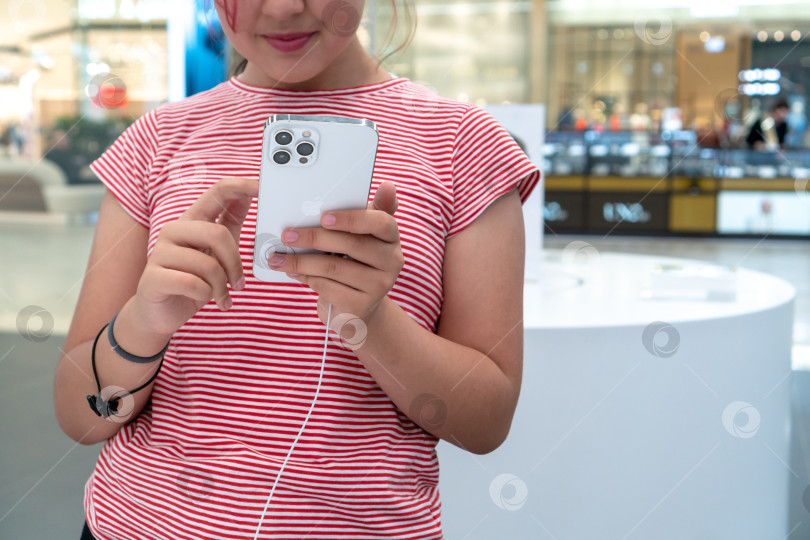 Скачать Очаровательная маленькая девочка держит в руках Apple iPhone 12 Pro Max серебристого цвета в Apple Store. Лица не видно. Россия, Татарстан, 10 июня 2021 года фотосток Ozero