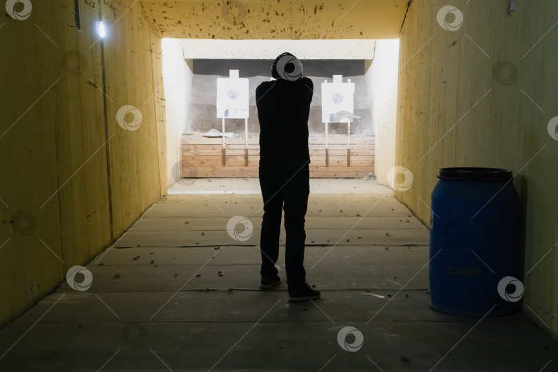 Скачать Мужчина в тире стреляет из пистолета GLOCK 19, вид сзади. o держит пистолет в руках, целясь в сторону от камеры с небольшой глубиной резкости. Россия, Татарстан, 29 сентября 2019 года. фотосток Ozero