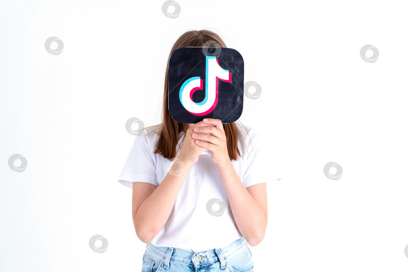 Скачать подросток белой расы держит в руках картинку с логотипом tiktok на белом фоне. Подростки увлекаются новыми технологическими тенденциями - концепцией молодежи, технологий, общения и дружбы. Турция, Стамбул, 29 мая 2022 года. фотосток Ozero