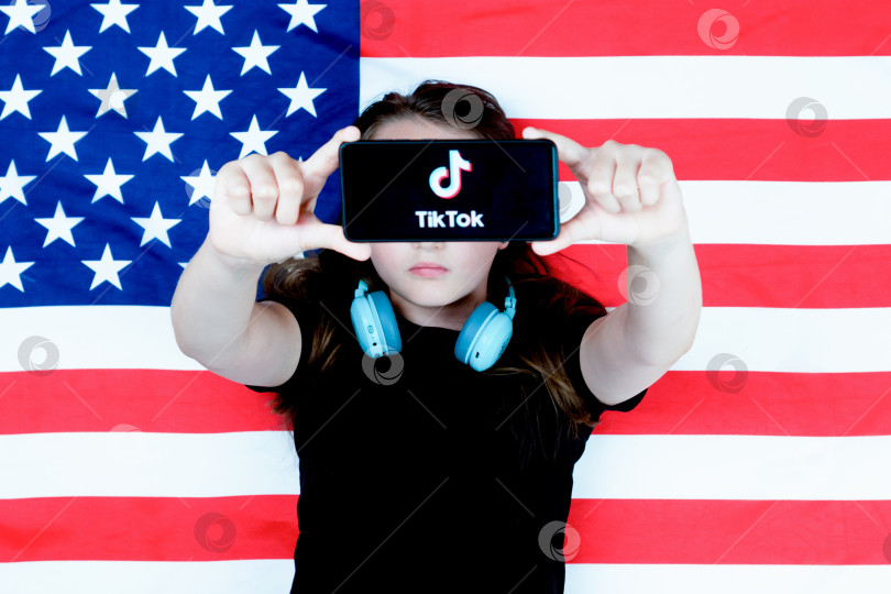 Скачать Подросток держит в руках смартфон с логотипом Tiktok на фоне американского флага. Избирательный подход. Дональд Трамп намерен запретить Tiktok в США. Россия, Казань - 08 августа 2020 г. фотосток Ozero