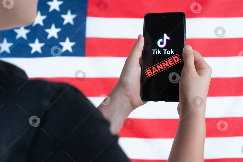 Скачать Подросток держит в руках смартфон с логотипом Tiktok на фоне американского флага. Избирательный подход. Дональд Трамп намерен запретить Tiktok в США. Россия, Казань - 08 августа 2020 г. фотосток Ozero