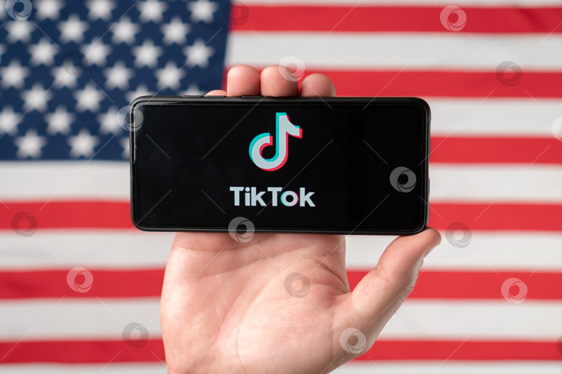 Скачать Логотип приложения Tiktok на смартфоне на фоне американского флага. Дональд Трамп намерен запретить Tiktok в США. Россия, Казань - 08 августа 2020 г. фотосток Ozero