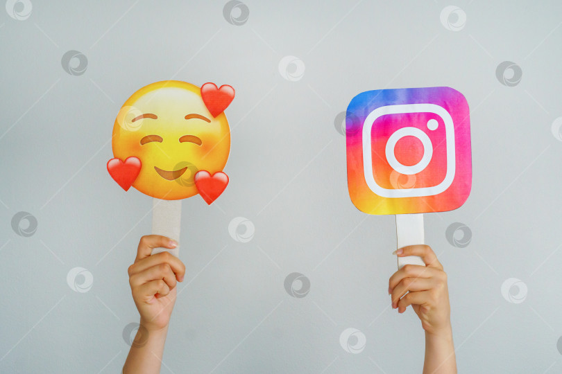 Скачать Девушка держит в руках значок с логотипом Instagram и эмодзи с улыбкой и сердечками, выделенными на сером фоне. Instagram - самая любимая и лучшая концепция социальной сети. Турция, Стамбул, 17 сентября 2024 года. фотосток Ozero