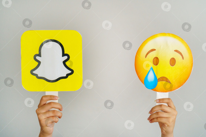 Скачать Девушка держит в руках значок с логотипом Snapchat и грустным плачущим эмодзи. Социальная сеть Snapchat теряет популярность. Турция, Стамбул, 17 сентября 2024 года. фотосток Ozero