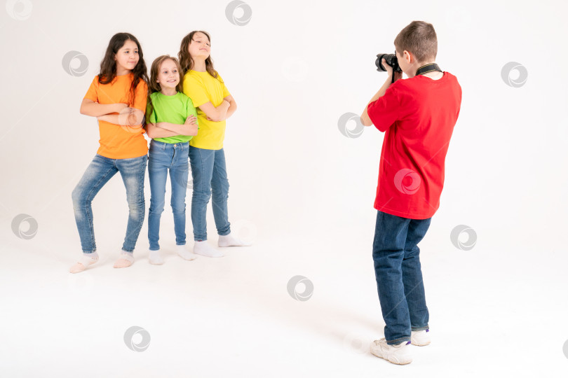 Скачать Молодой фотограф фотографирует трех симпатичных девушек в ярких футболках на белом фоне в студии. Молодой фотограф и блогер фотосток Ozero