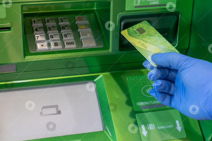Скачать Банковская карта Visa в руке в медицинской защитной перчатке на фоне банкомата. Россия, Татарстан, 18 апреля 2020 г. фотосток Ozero