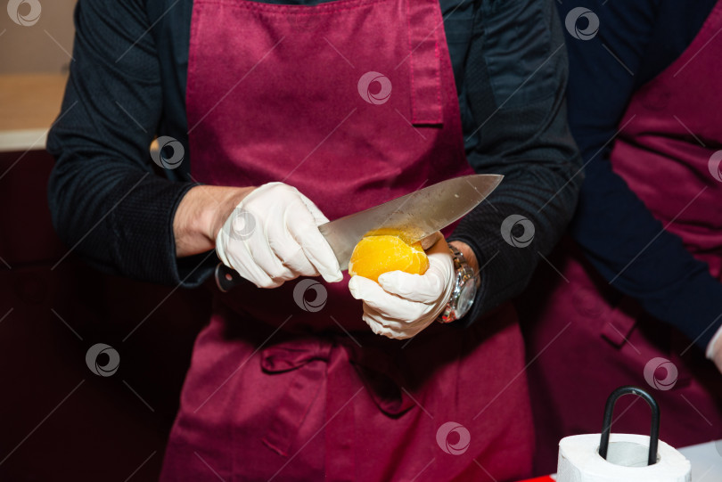 Скачать Шеф-повар нарезает апельсин ножом на кухне. фотосток Ozero