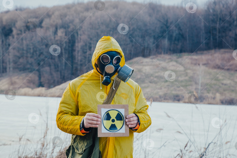 Скачать Человек в черном противогазе и желтом защитном костюме стоит в загрязненном радиацией лесу на фоне радиационных осадков фотосток Ozero