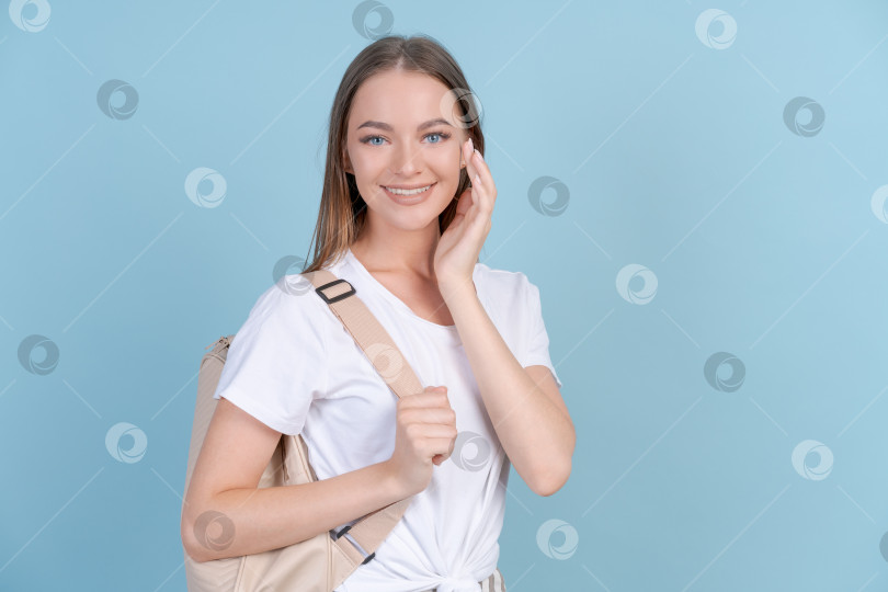 Скачать Счастливая студентка в легкой повседневной одежде стоит, улыбаясь, на синем фоне фотосток Ozero