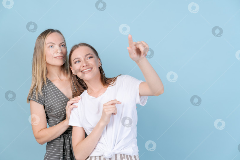 Скачать Веселая молодая взрослая дочь указывает рукой в сторону мамы, мама обнимает ее фотосток Ozero