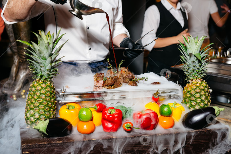 Скачать Шеф-повар поливает мясо соусом, разложив сухой лед. фотосток Ozero