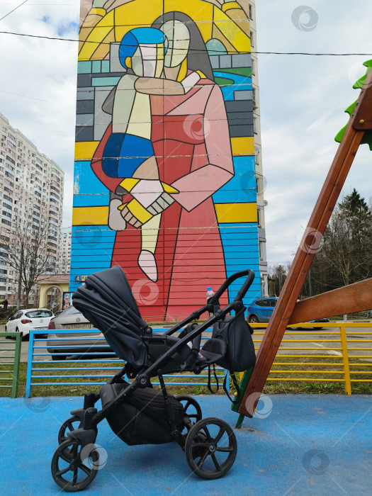 Скачать Детская коляска на площадке на фоне огромного граффити Матери и ребенка на стене высокого дома фотосток Ozero