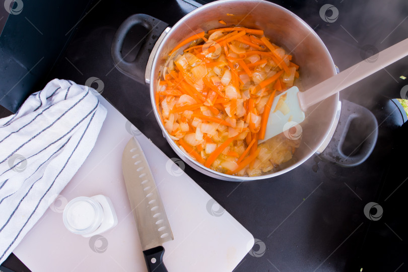 Скачать Запеканка с тушеным луком и морковью на пару на черной плите с ножом и полотенцем фотосток Ozero
