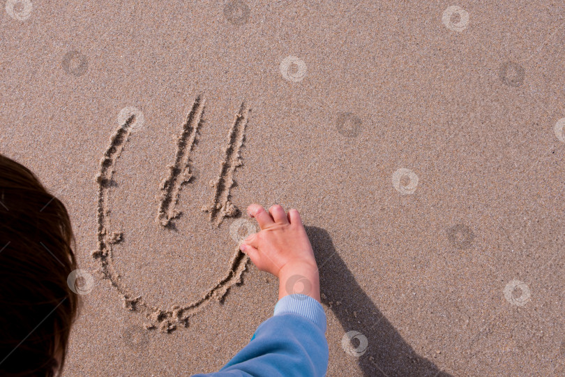 Скачать Ребенок рисует смайлик на песке на пляже вручную фотосток Ozero