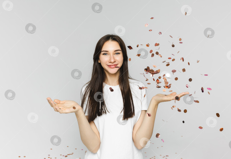 Скачать Фотография веселой девушки, бросающей звездочки и конфетти, на белом фоне. женщина, ловящая конфетти фотосток Ozero
