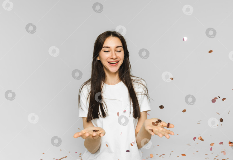 Скачать Фотография веселой девушки, бросающей звездочки и конфетти, на белом фоне. женщина, ловящая конфетти фотосток Ozero