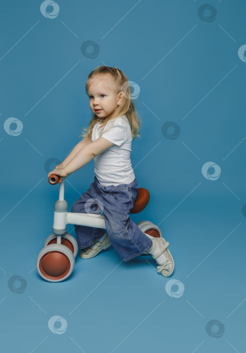 Скачать маленькая девочка 2-3 лет в белой футболке сидит на велотренажере в студии. летние развлечения на свежем воздухе для детей фотосток Ozero