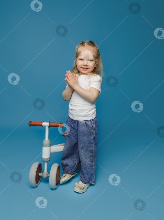 Скачать маленькая девочка 2-3 лет в белой футболке сидит на велотренажере в студии. летние развлечения на свежем воздухе для детей фотосток Ozero