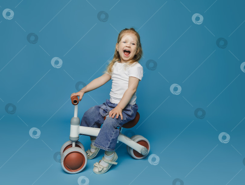 Скачать маленькая девочка 2-3 лет в белой футболке сидит на велотренажере в студии. летние развлечения на свежем воздухе для детей фотосток Ozero