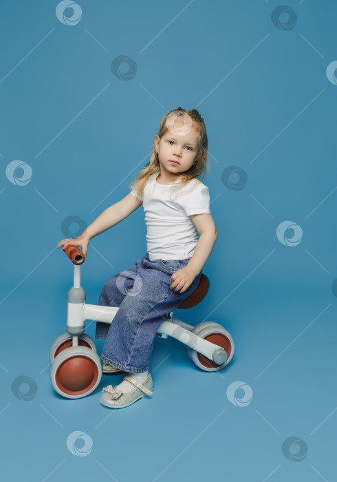 Скачать маленькая девочка 2-3 лет в белой футболке сидит на велотренажере в студии. летние развлечения на свежем воздухе для детей фотосток Ozero