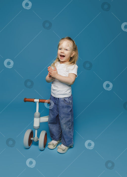 Скачать маленькая девочка 2-3 лет в белой футболке сидит на велотренажере в студии. летние развлечения на свежем воздухе для детей фотосток Ozero