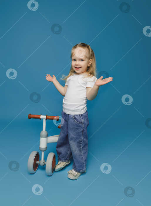 Скачать маленькая девочка 2-3 лет в белой футболке сидит на велотренажере в студии. летние развлечения на свежем воздухе для детей фотосток Ozero