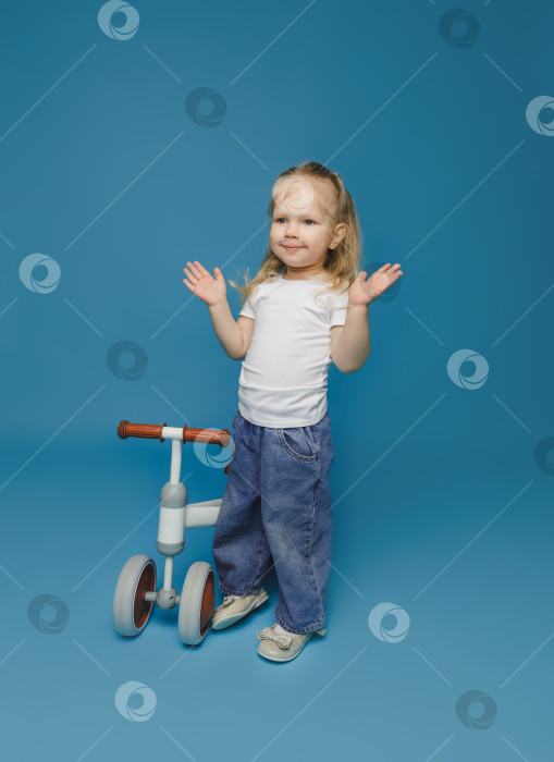 Скачать маленькая девочка 2-3 лет в белой футболке сидит на велотренажере в студии. летние развлечения на свежем воздухе для детей фотосток Ozero
