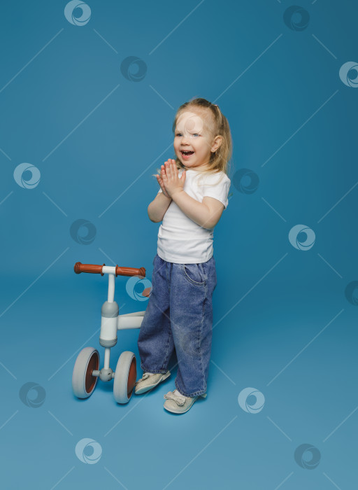 Скачать маленькая девочка 2-3 лет в белой футболке сидит на велотренажере в студии. летние развлечения на свежем воздухе для детей фотосток Ozero