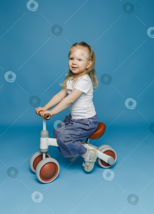 Скачать маленькая девочка 2-3 лет в белой футболке сидит на велотренажере в студии. летние развлечения на свежем воздухе для детей фотосток Ozero