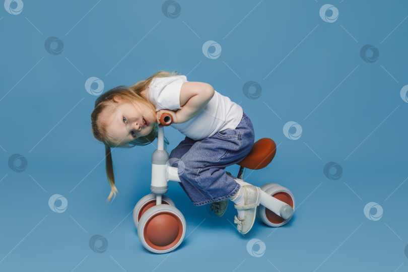 Скачать маленькая девочка 2-3 лет в белой футболке сидит на велотренажере в студии. летние развлечения на свежем воздухе для детей фотосток Ozero