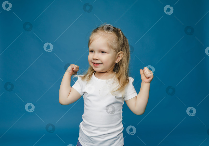 Скачать Фотография жизнерадостной счастливой девочки 2-3 лет, показывающей большой палец вверх, что означает "рекомендуется", выделенная на синем фоне. фотосток Ozero